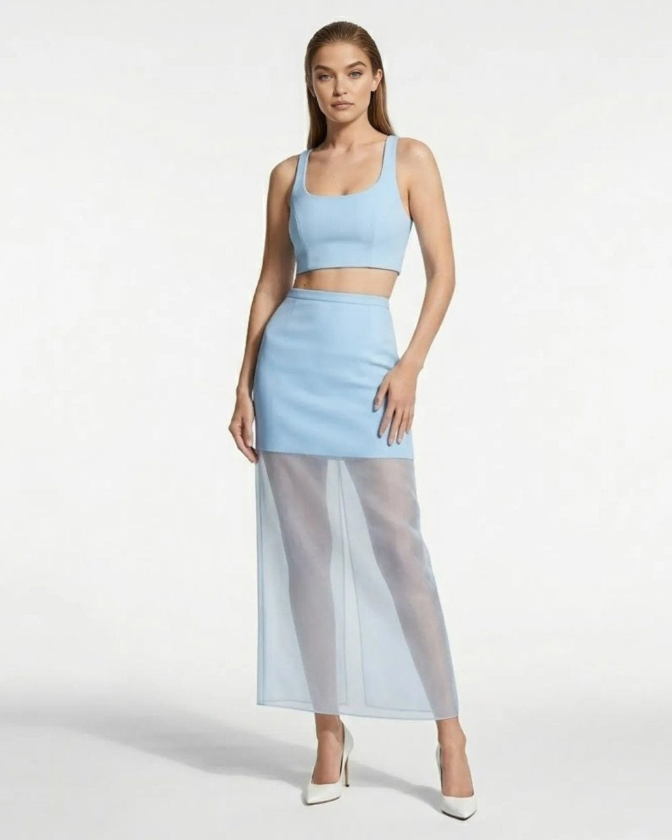 Model wearing an elegant light blue designer cocktail skirt with a transparent maxi hem paired with a matching crop top and white heels.