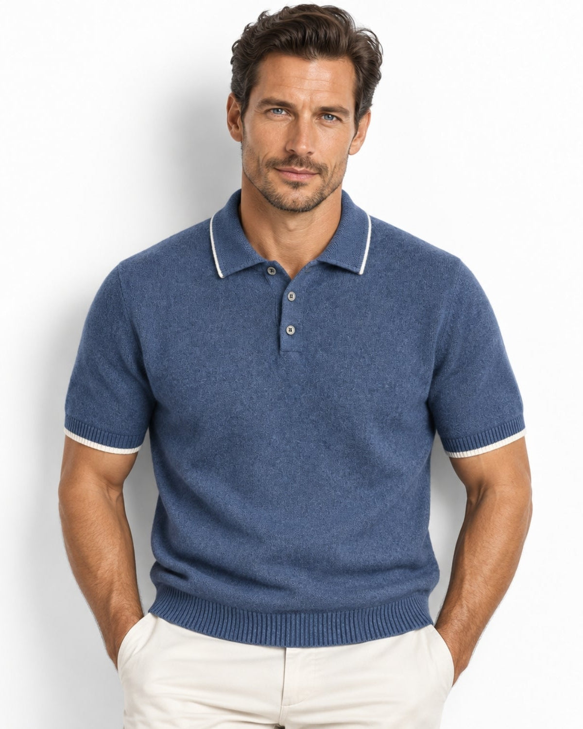 A man wearing a blue short-sleeve knit polo shirt with white contrast trim on the collar and sleeve cuffs, paired with off-white trousers, against a plain white background.