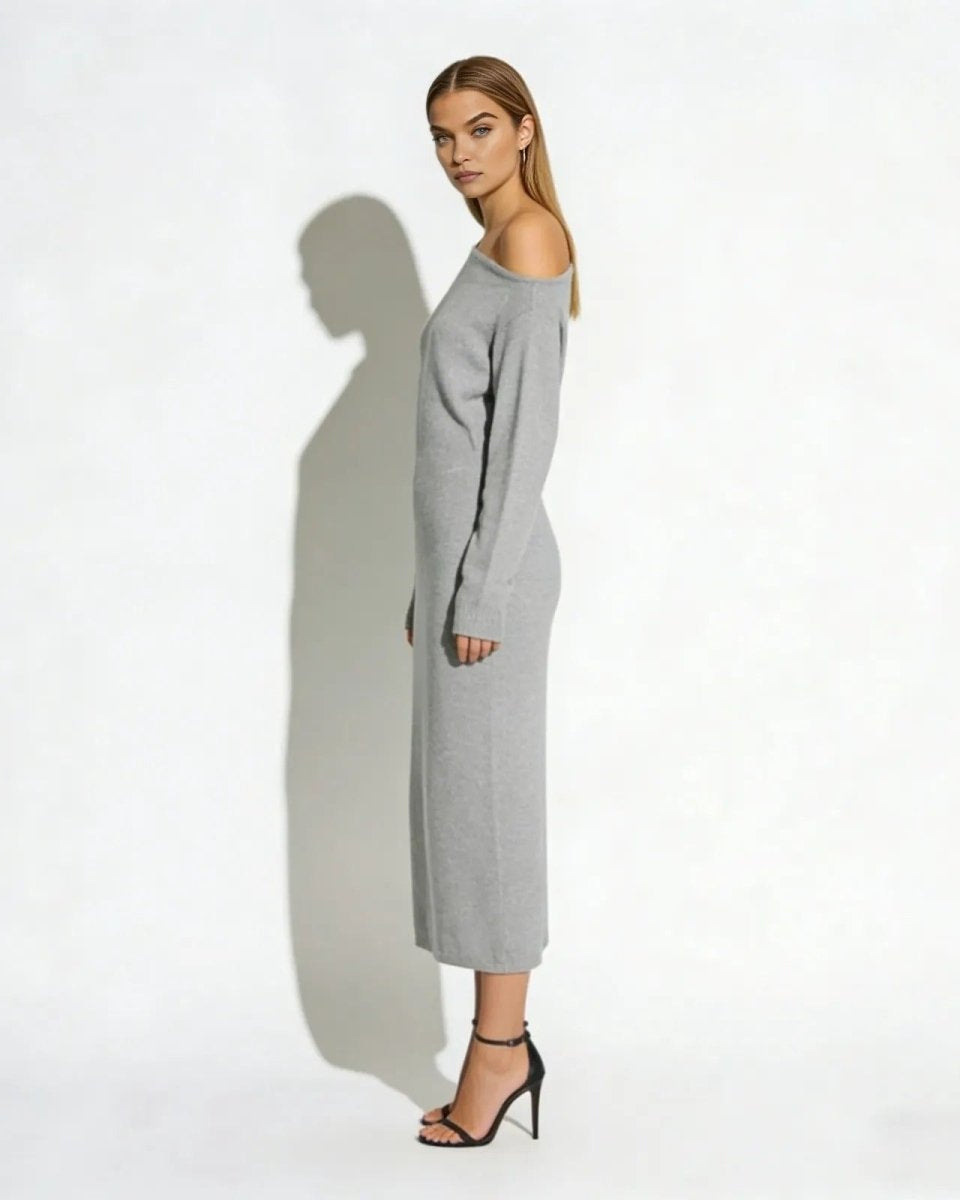 Side profile of a model in a light grey long sleeve asymmetrical sweater dress with black heels.