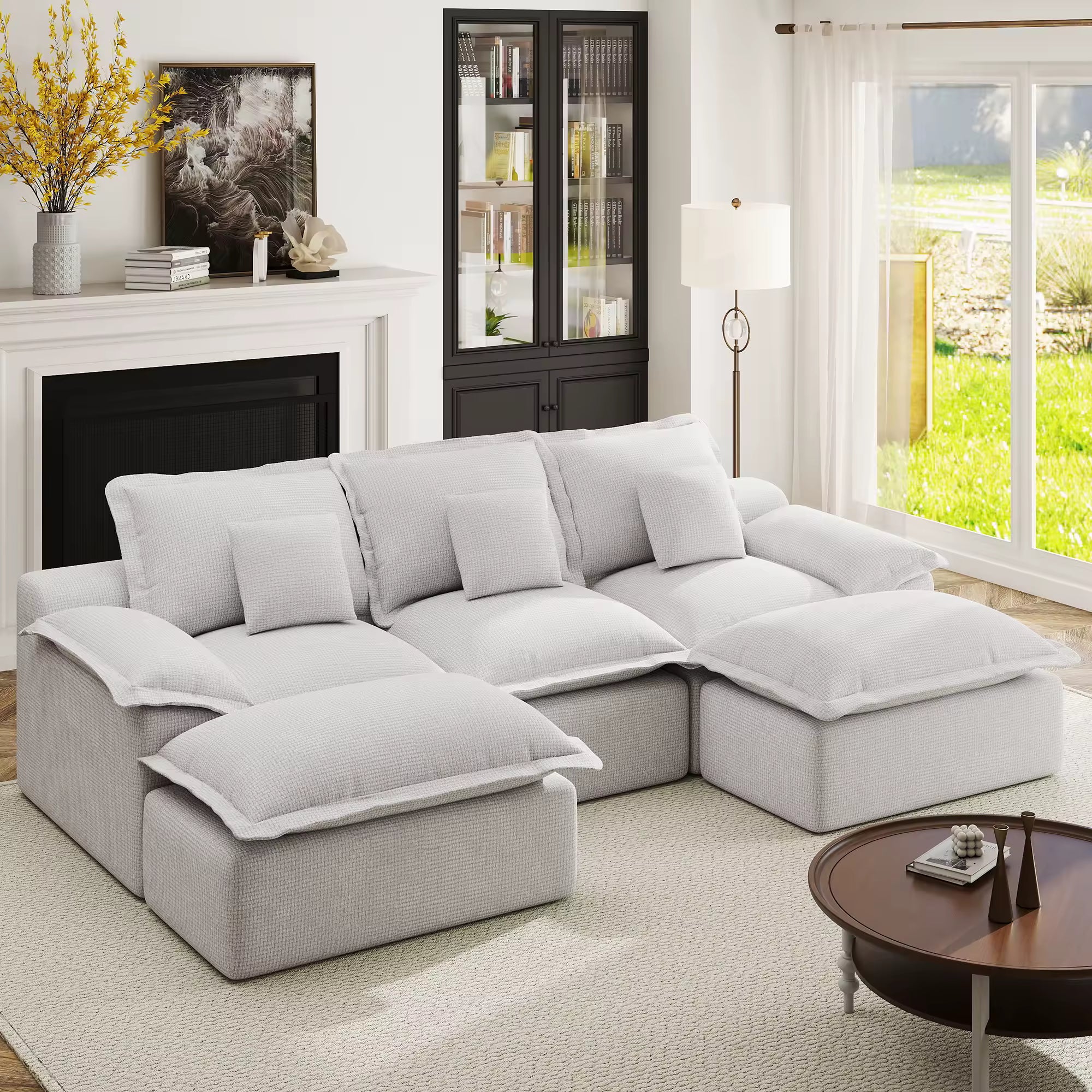 Light grey modular sectional sofa with plush cushions and dual ottomans in a bright living room with a fireplace.