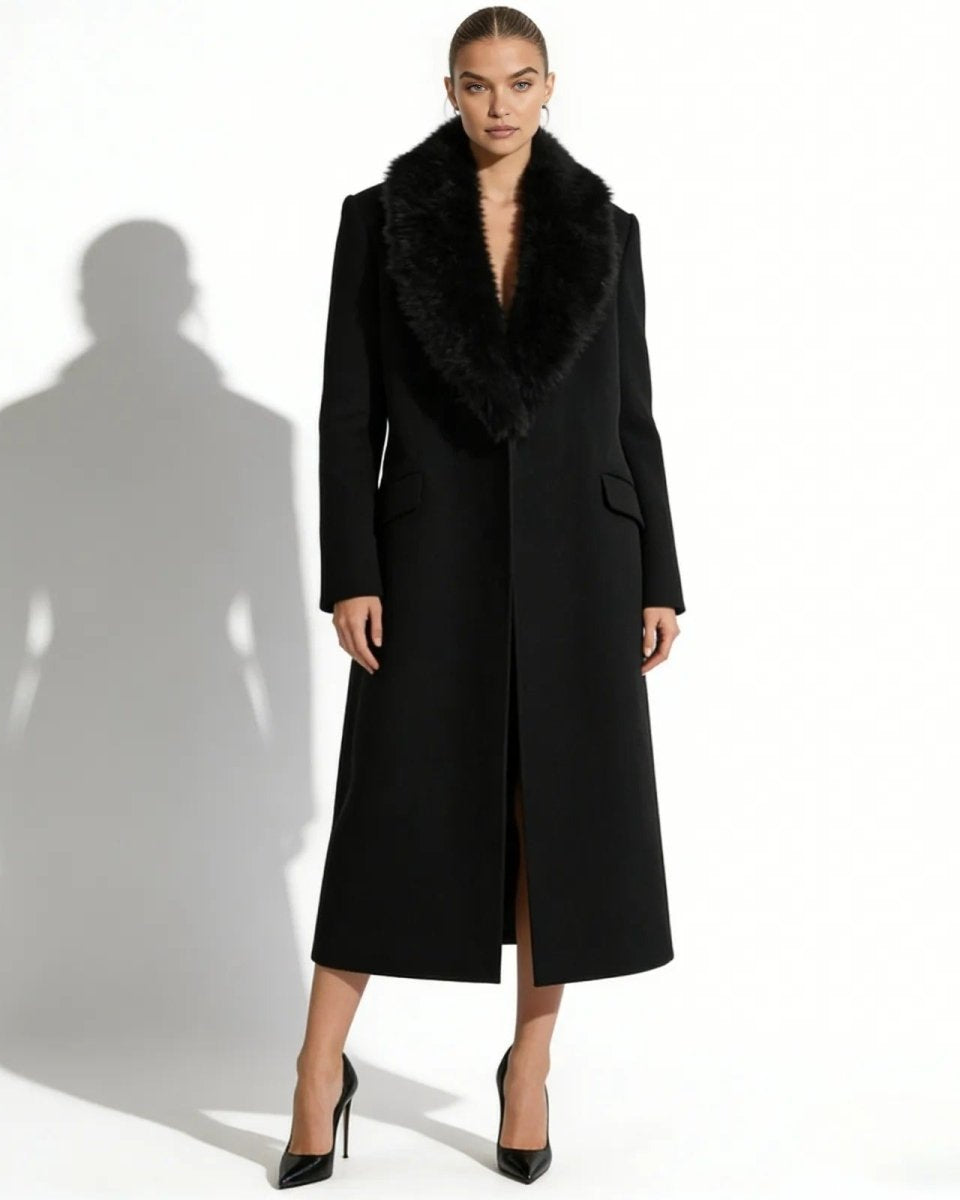 Model facing forward in a long black wool overcoat with a wide faux fur collar, styled open without a belt.