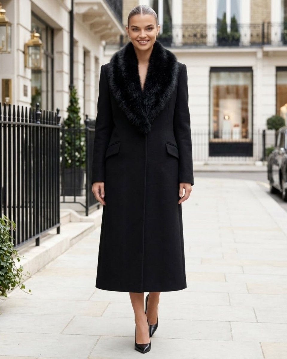 A woman wearing a long black wool coat with a luxurious black fur collar walks down a paved city street lined with elegant buildings.