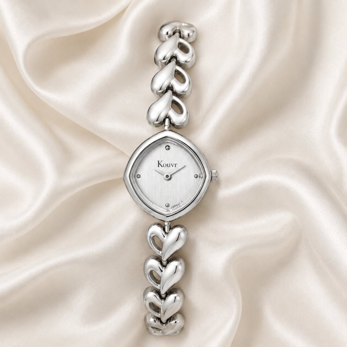 Beautiful product photography featuring the Kouvr silver ladies timepiece lying on luxurious, draped pearl-colored satin material.