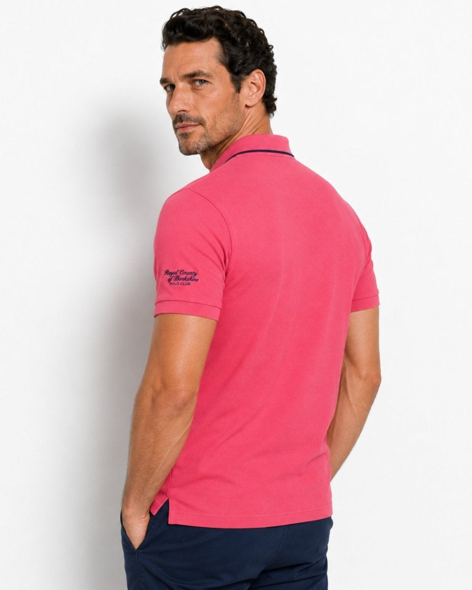 Man wearing a pink polo shirt with a visible brand logo on a light gray background