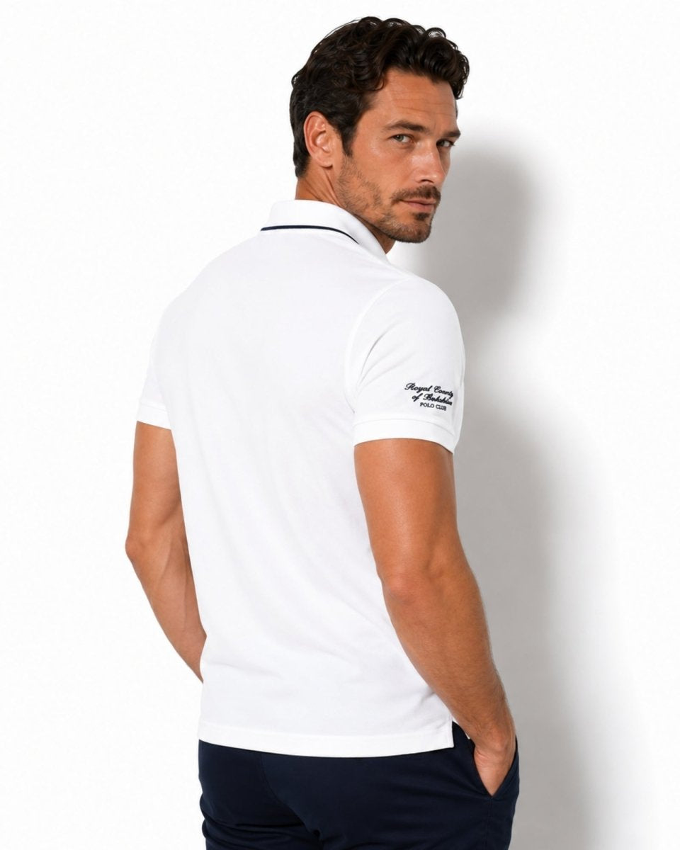 Man wearing a white polo shirt with a brand logo on a plain background