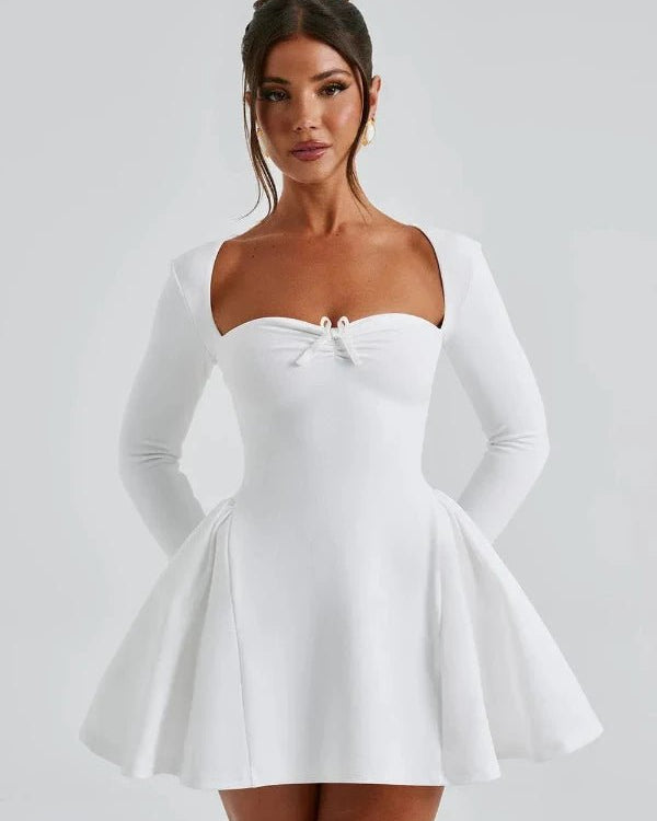 Woman wearing a white dress with long sleeves on a plain background