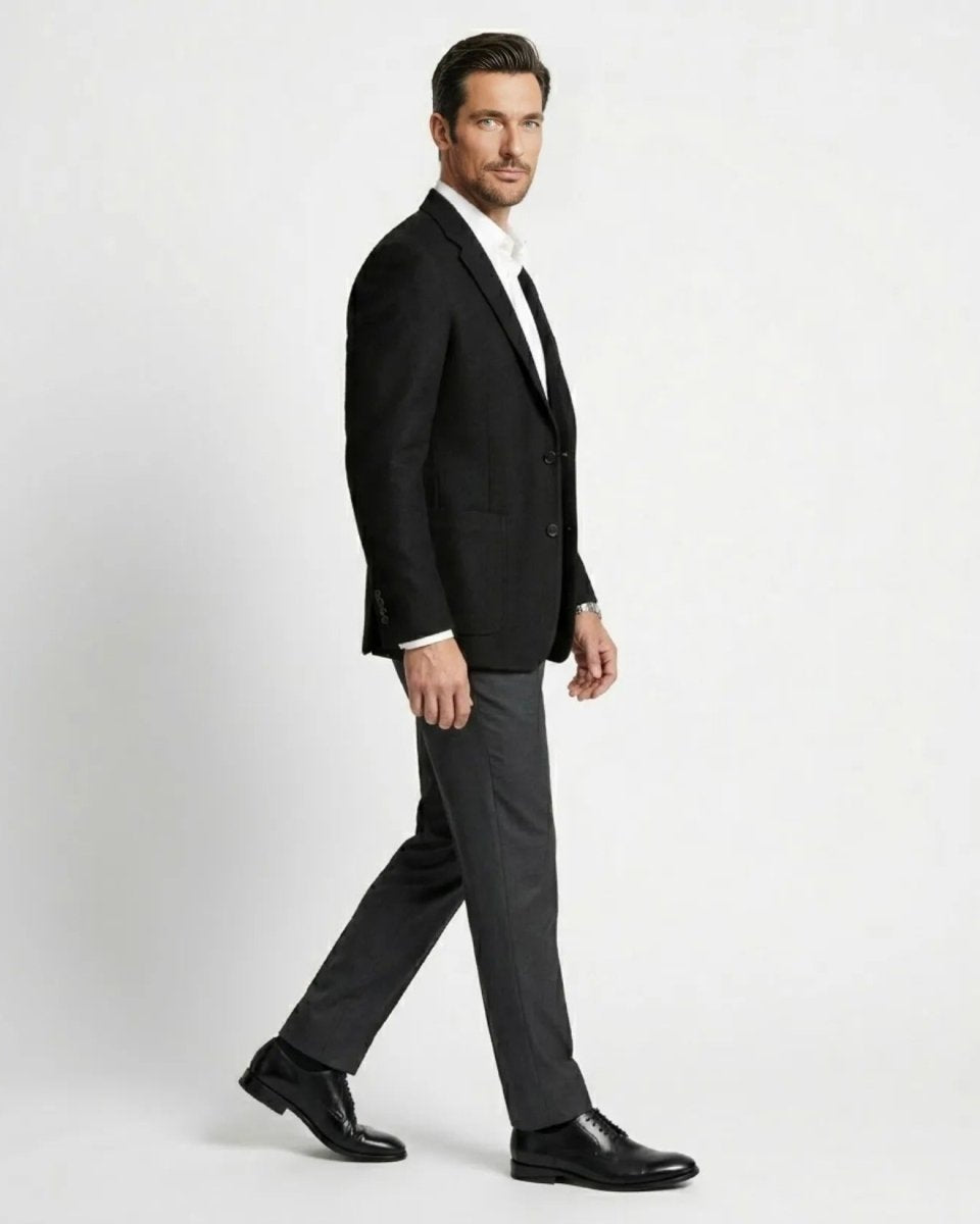 Side profile of male model walking wearing a black tailored patch pocket suit jacket.