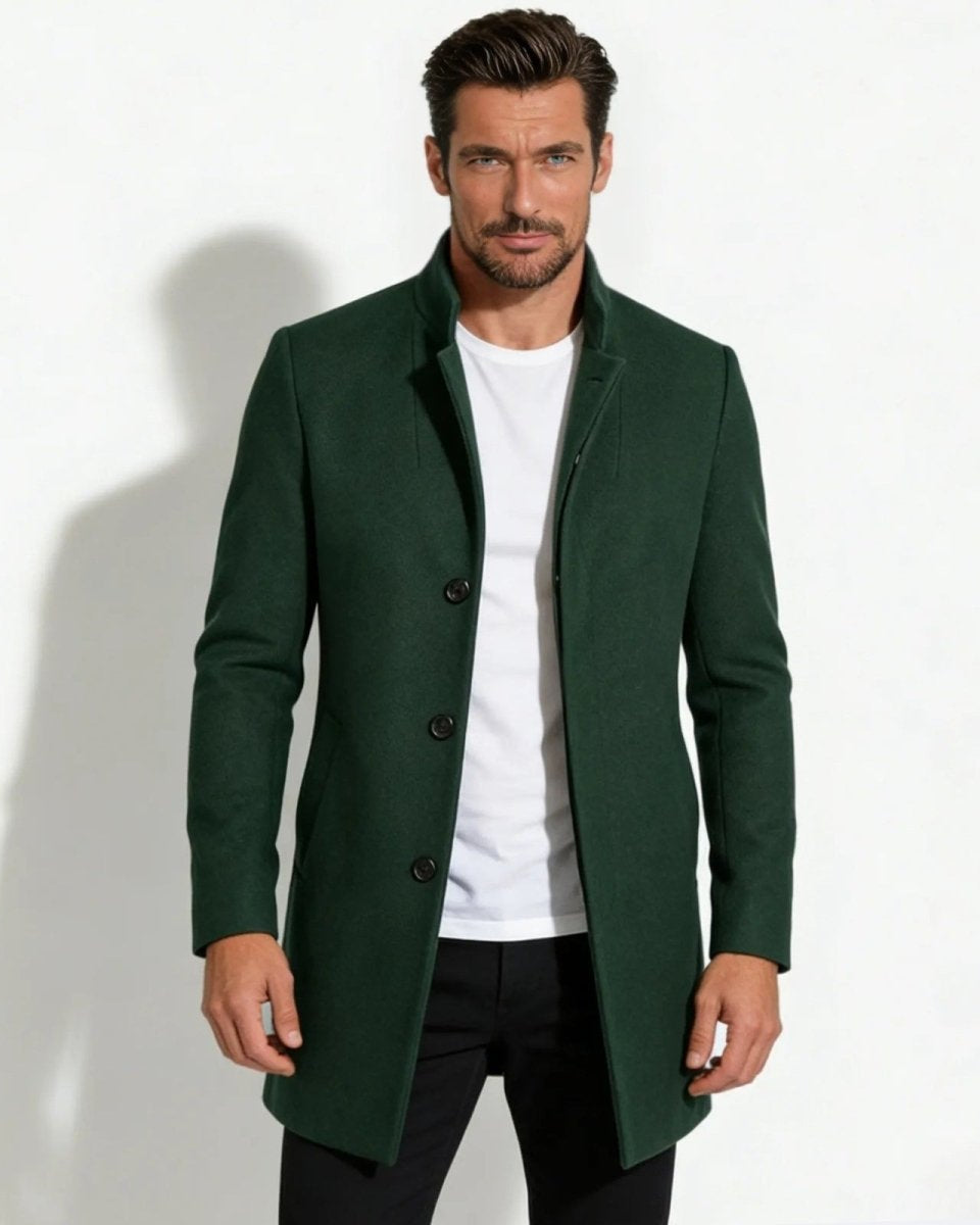 Model wearing a dark forest green men's wool stand collar overcoat, styled with a white t-shirt and black trousers.