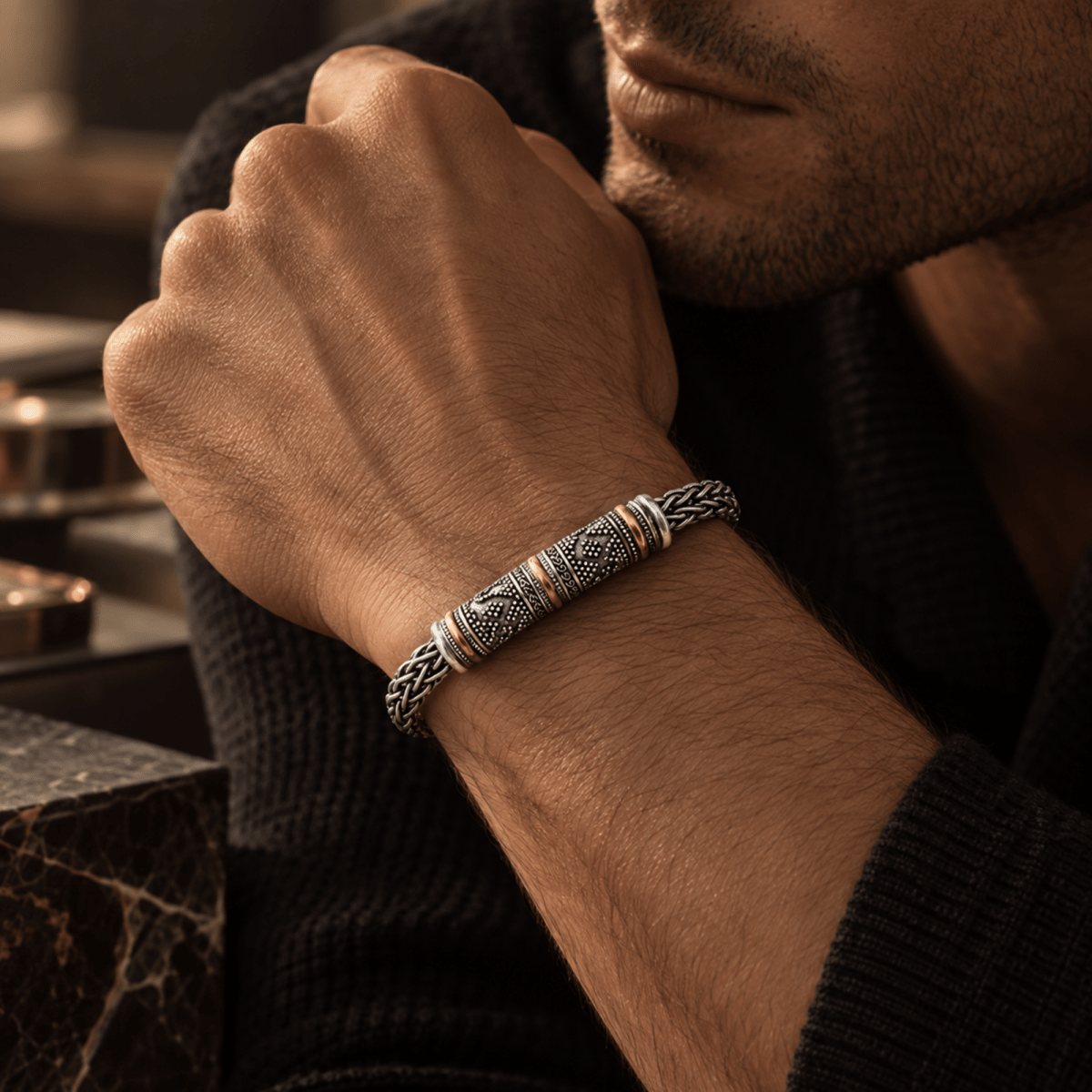 A close-up lifestyle shot of a man wearing a silver and gold textured cuff bracelet on his wrist, resting his chin in thought.