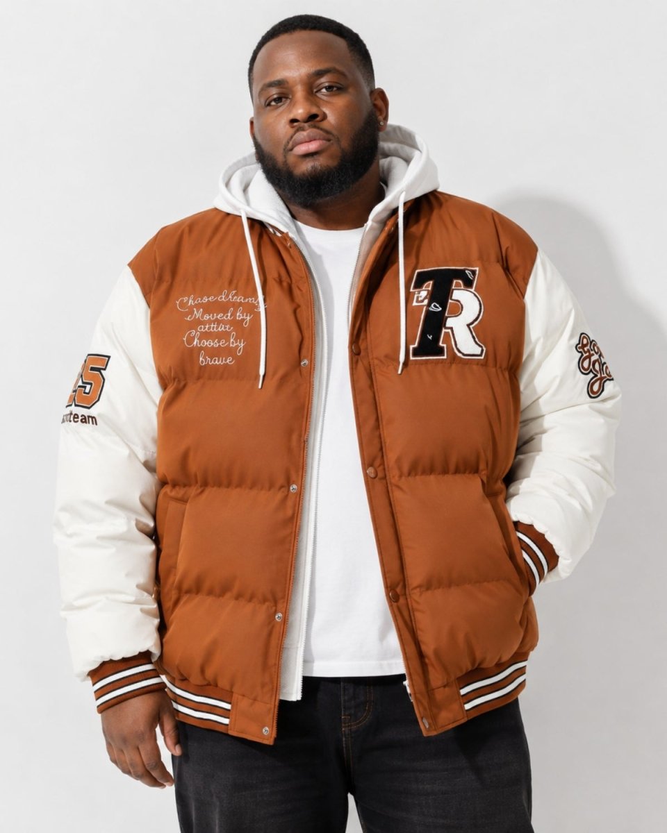 A man wearing a brown and white varsity-style puffer jacket with a white hoodie underneath, photographed against a plain light gray studio background.