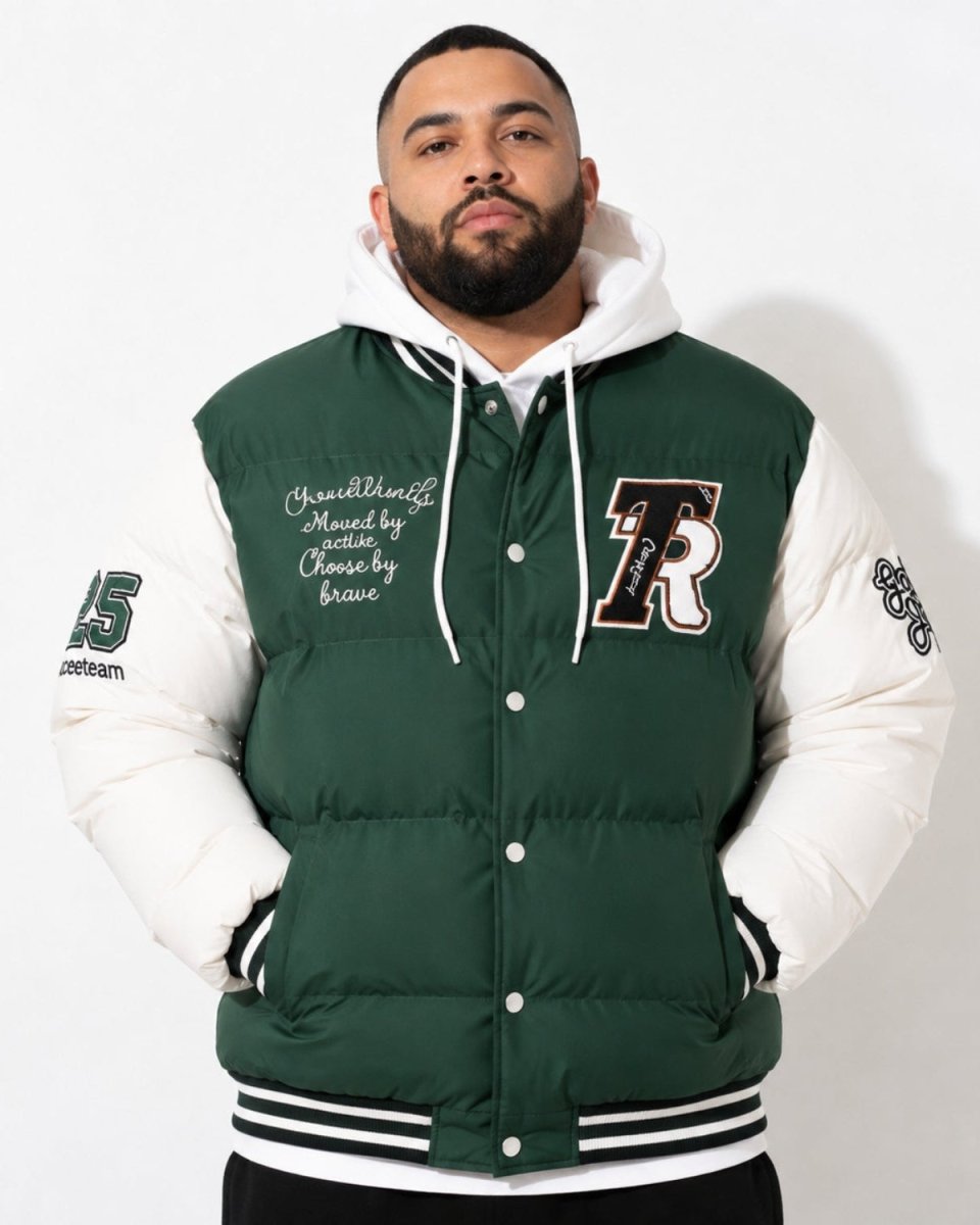 A man wearing a dark green and white varsity puffer jacket with a white hoodie underneath, standing against a plain white background.