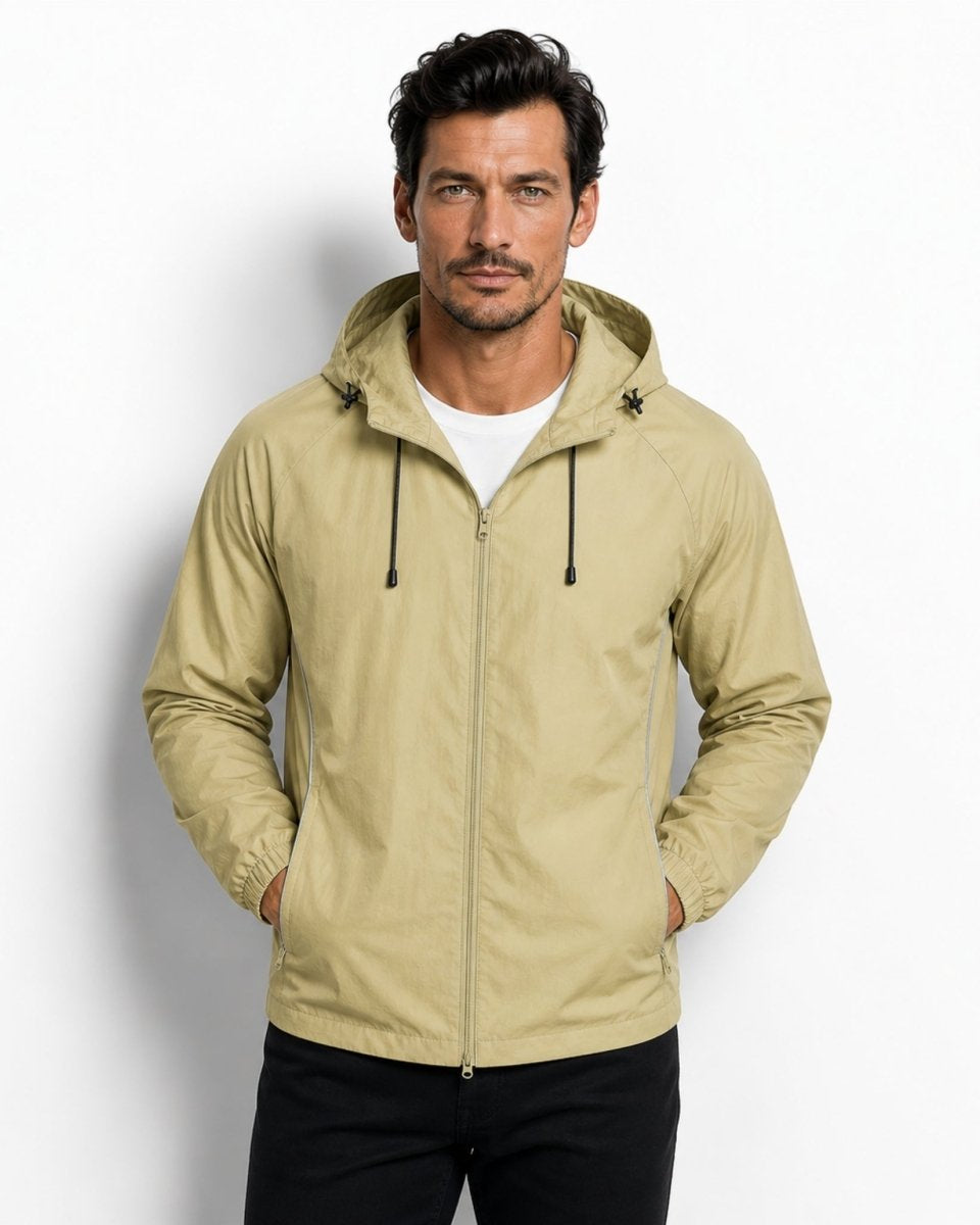 Man wearing premium light army green lightweight hooded windbreaker jacket with hands in pockets against a white studio background.