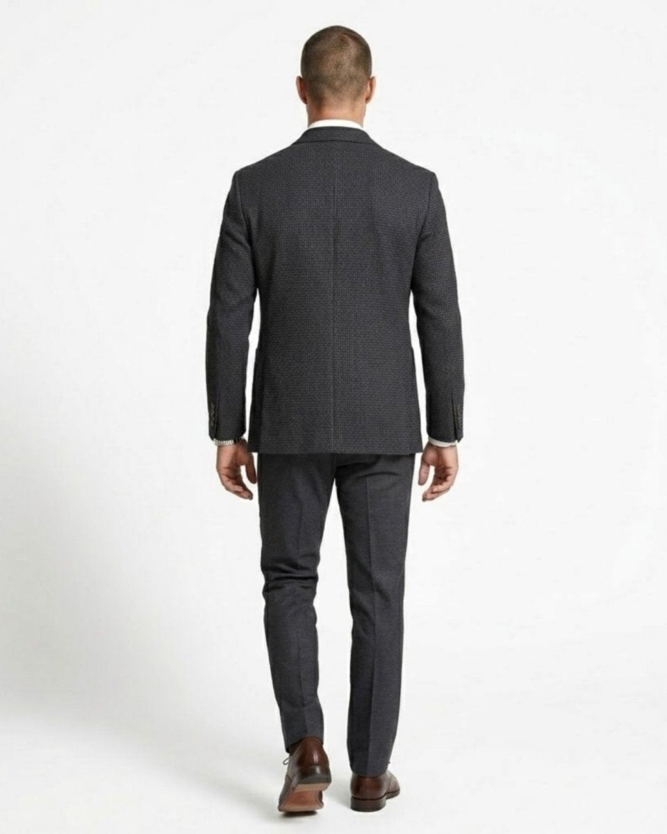 Full body back view of a man walking away wearing a tailored plaid suit jacket and grey trousers.