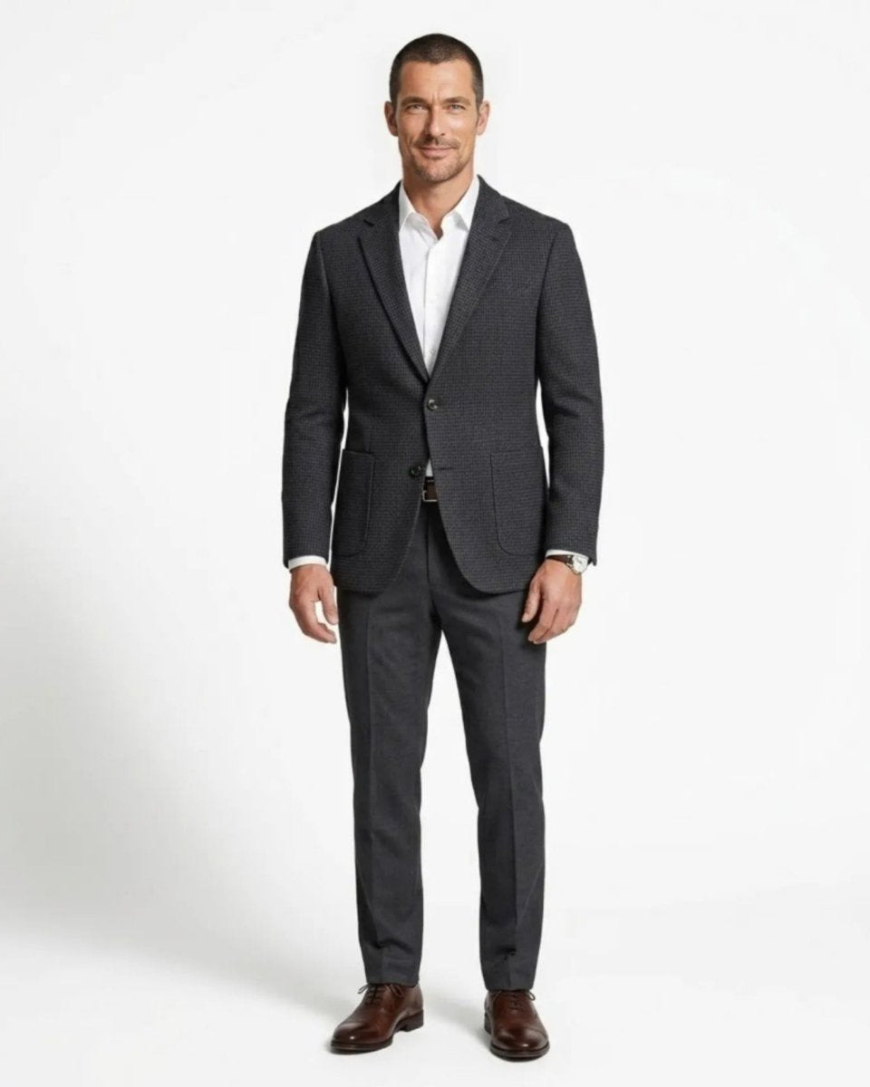 Full body front view of a male model wearing a plaid smart casual suit jacket with grey dress pants and brown shoes.