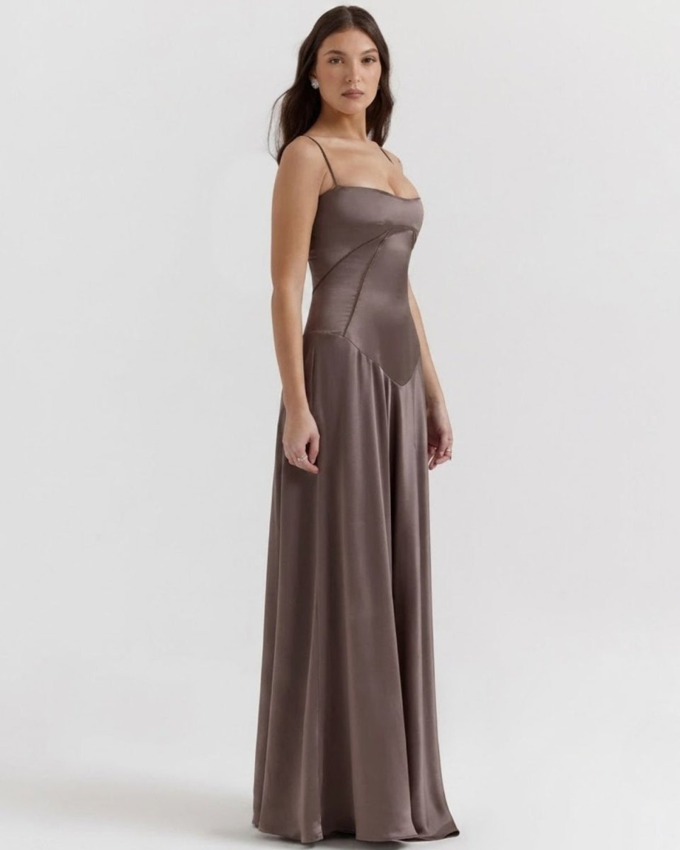 A woman modeling a floor-length satin bridesmaid dress in a muted taupe-brown color, standing against a plain light gray studio background.