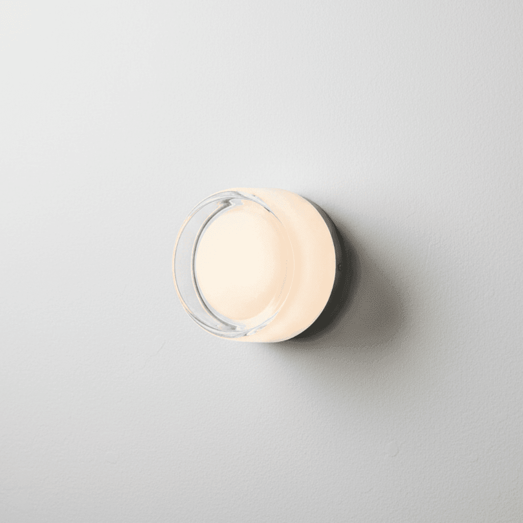 Close-up of a circular minimalist glass wall sconce emitting a warm amber glow against a textured beige plaster wall.