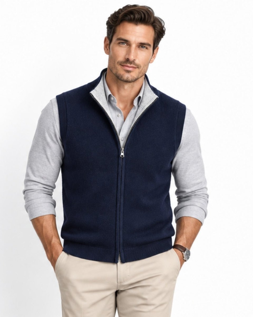 Handsome man wearing a navy luxury full zip cashmere blend sweater vest layered over a light grey shirt with hands in pockets.