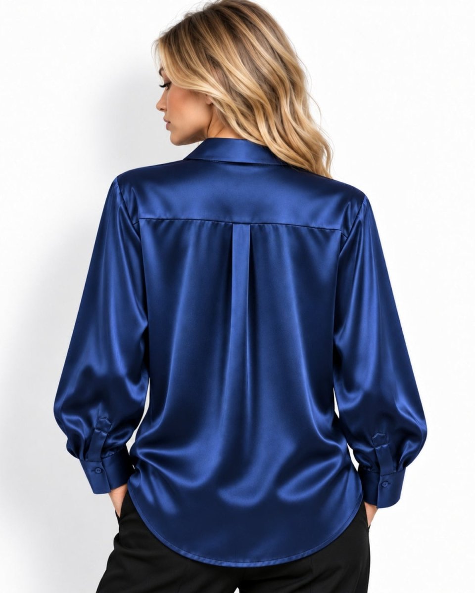 A woman shown from the back wearing a shiny royal blue silk button-up shirt and black pants, photographed against a plain white studio background.