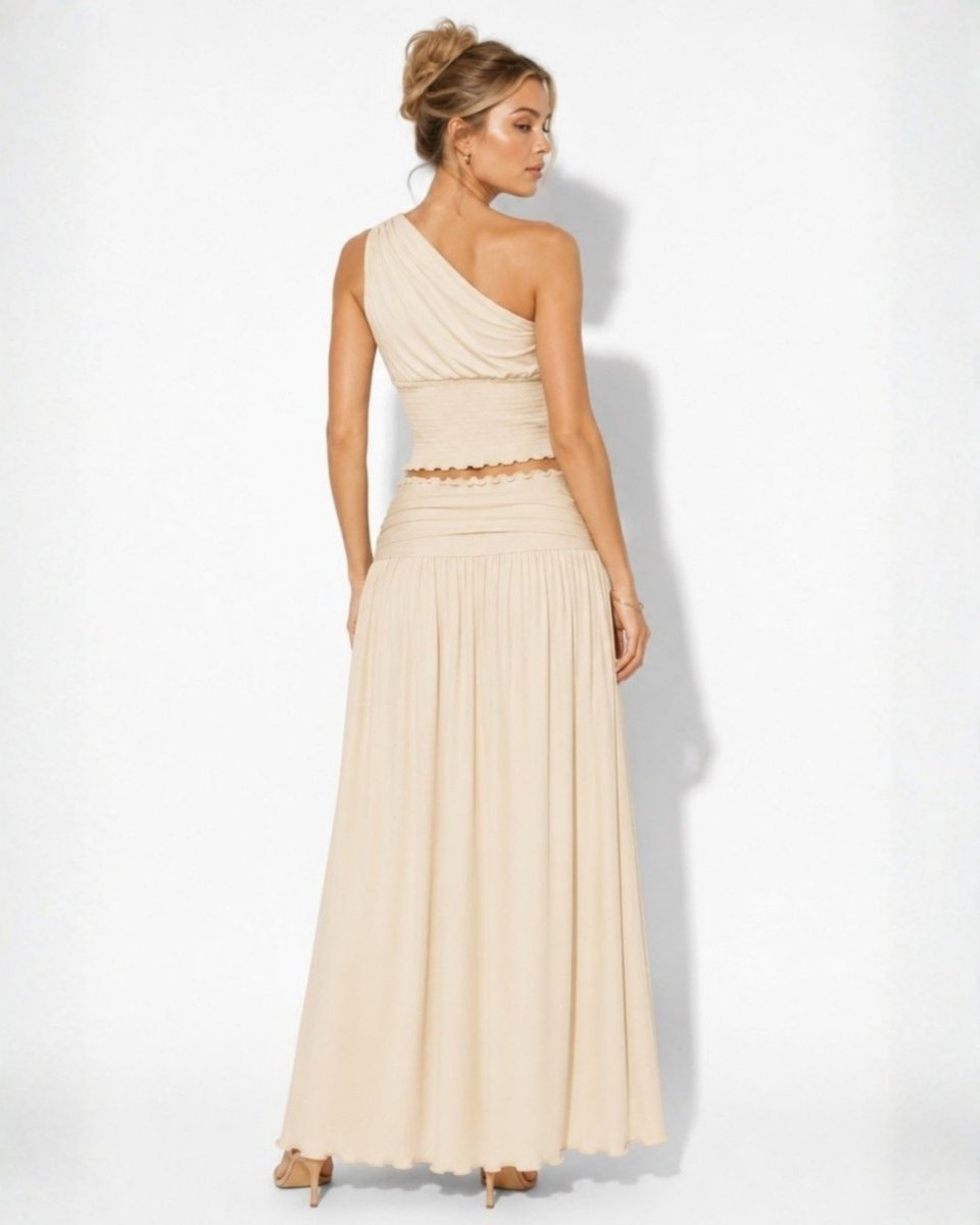 A woman modeling a one-shoulder maxi dress in a light beige or cream color, shown from a three-quarters back view against a plain white studio background.