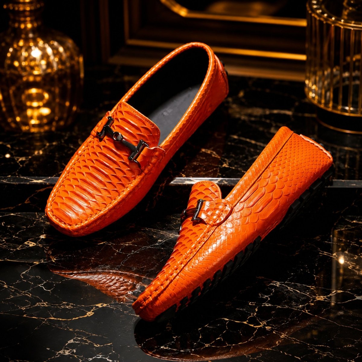 A pair of bright orange crocodile-embossed leather loafers with black decorative hardware, displayed on a black marble surface with a warm, golden ambient background.