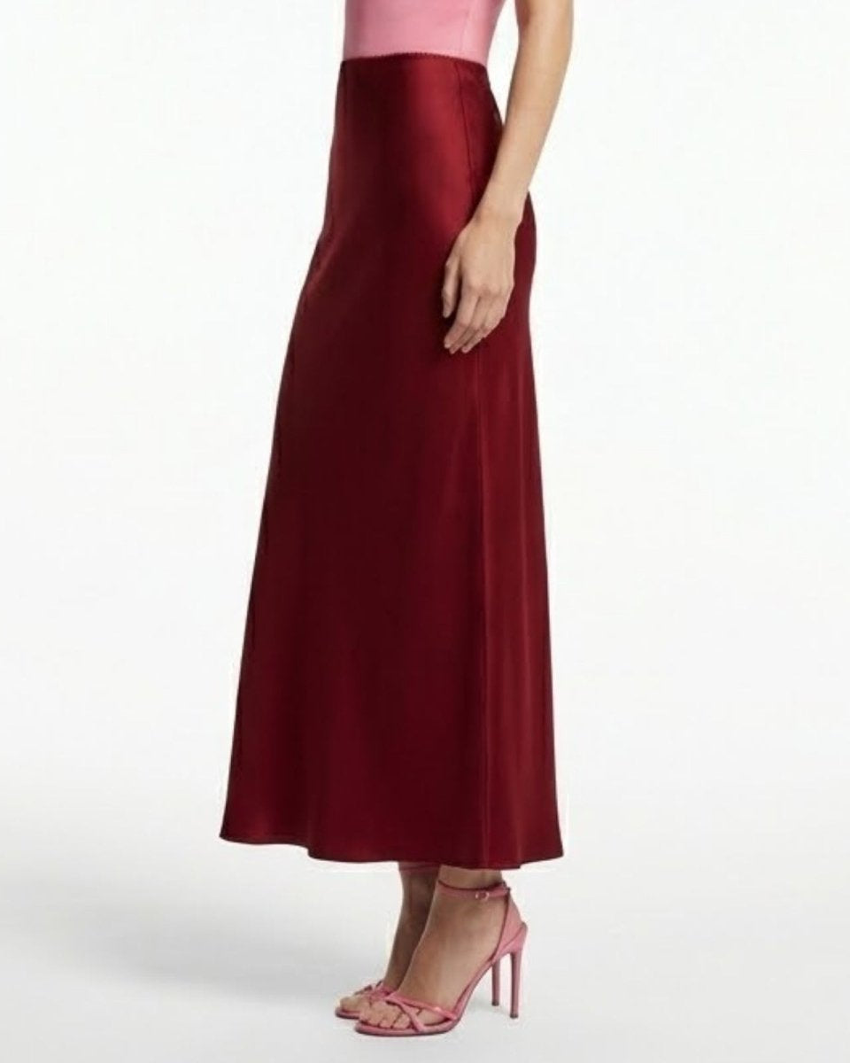 Close-up detail of the liquid satin fabric and fit of the high-waisted Ourania maxi skirt in deep red.