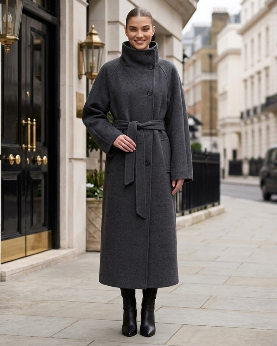 A woman wearing a dark gray wool-blend coat with a high mock neck and matching waist tie belt, standing on a city street.