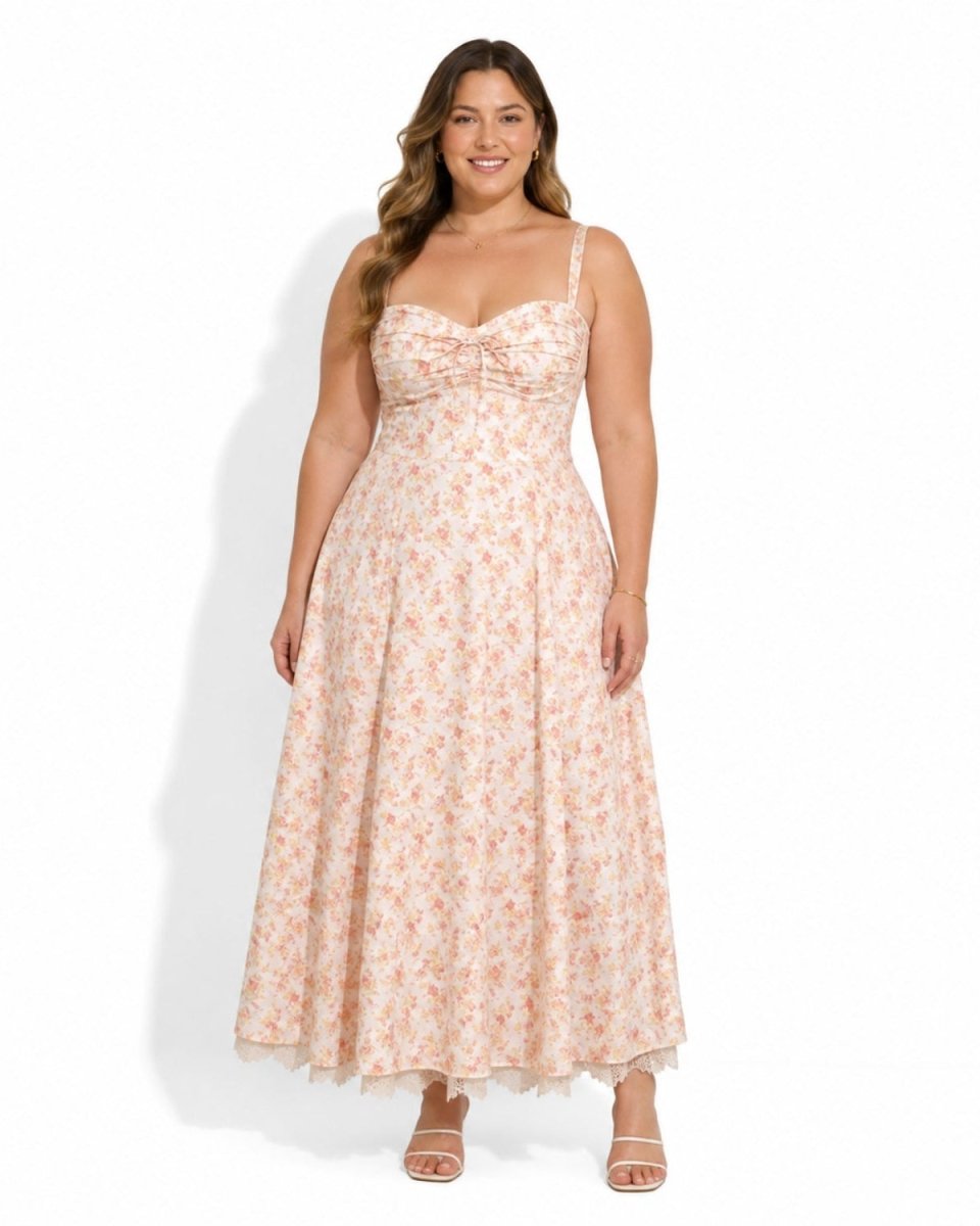 A woman modeling a sleeveless, floor-length floral maxi dress with thin straps and a sweetheart neckline, standing against a plain white studio background.