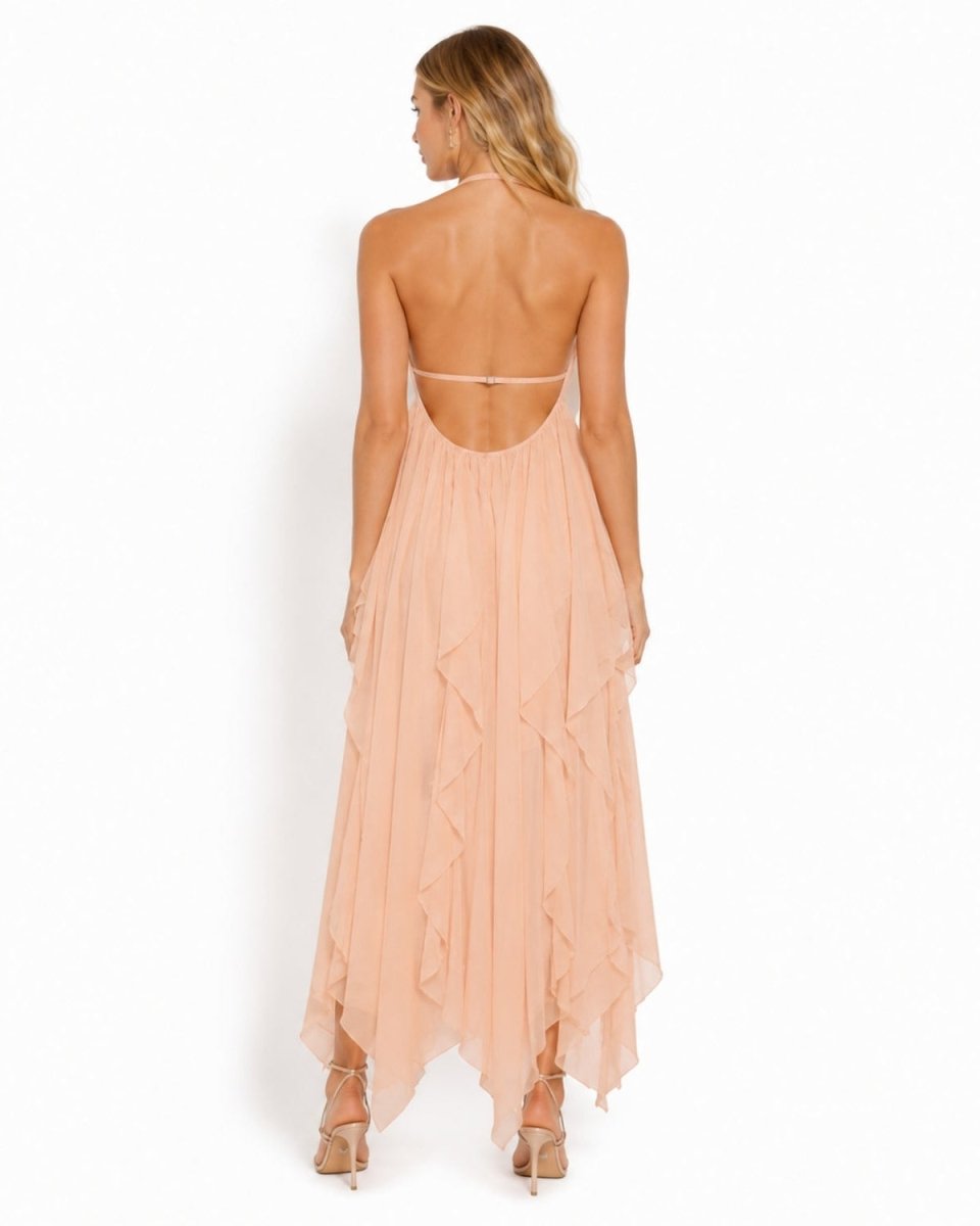 A woman viewed from the back wearing a peach-colored, strapless maxi dress with a ruffled tiered skirt and a thin waistband, paired with beige high-heeled sandals against a plain white background.