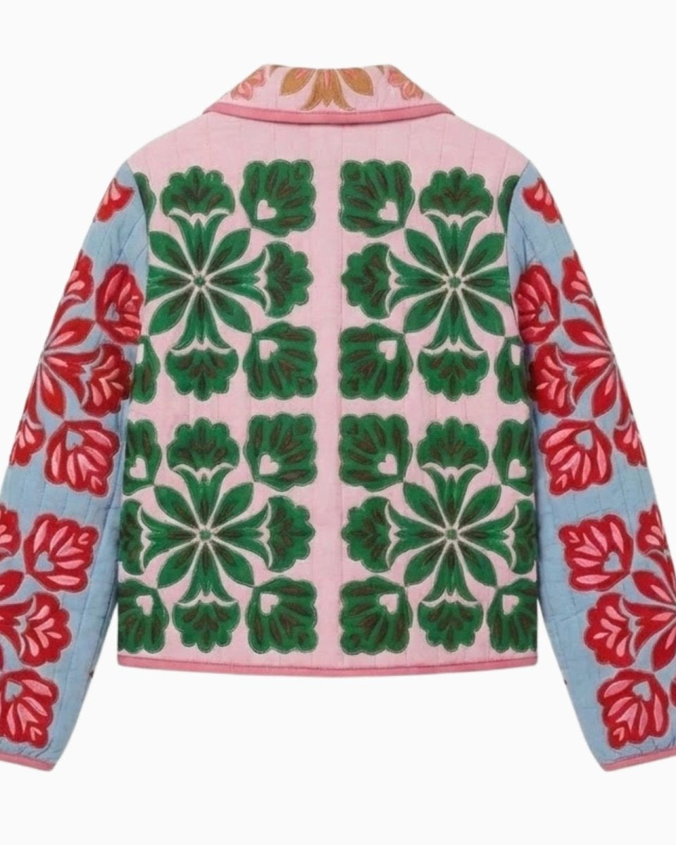 Flat lay showing the back of a quilted jacket with a repeating green floral tile pattern on a pink background and blue embroidered sleeves.