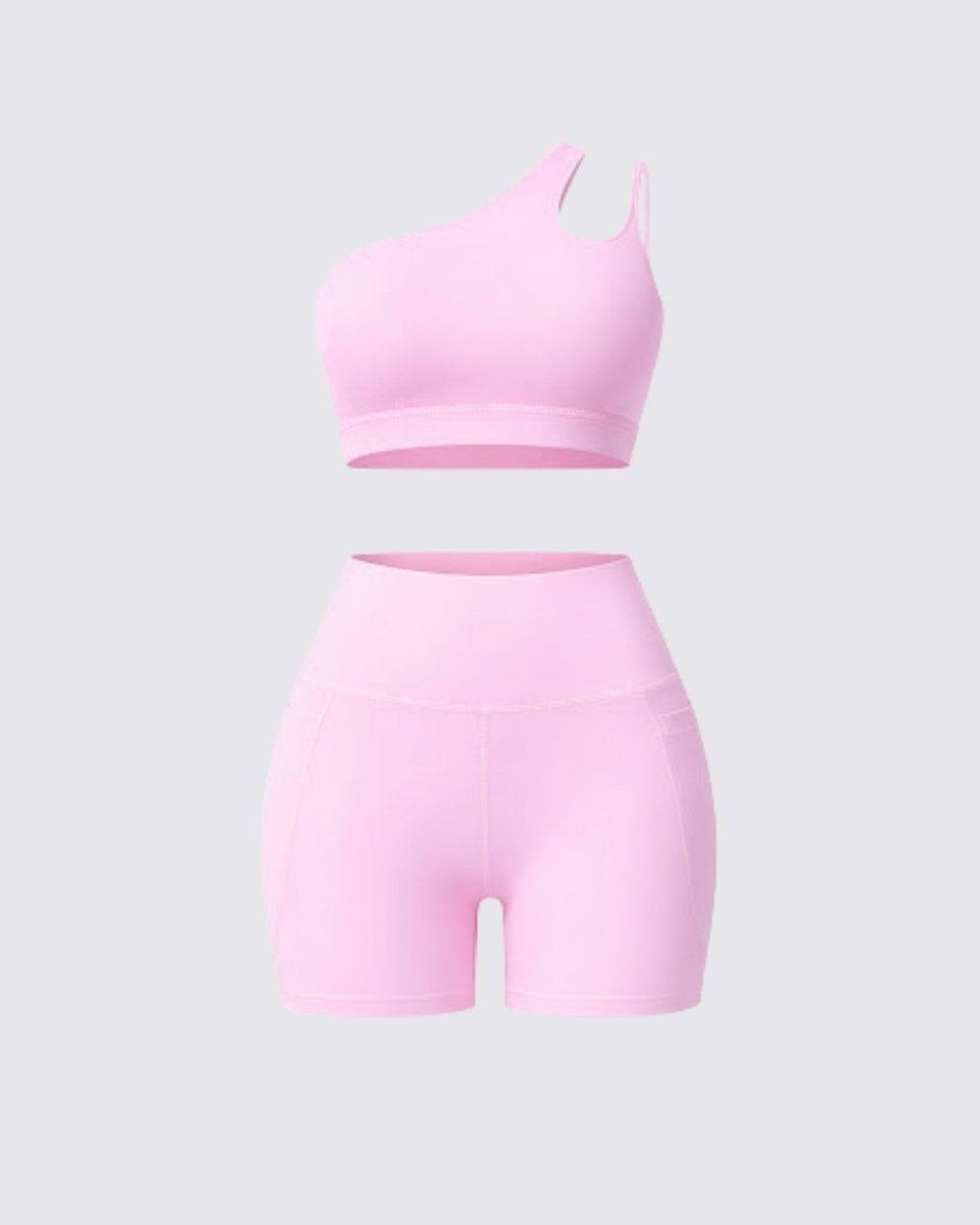 Front flatlay display of a pink two piece yoga outfit featuring a one shoulder workout top and high rise athletic shorts
