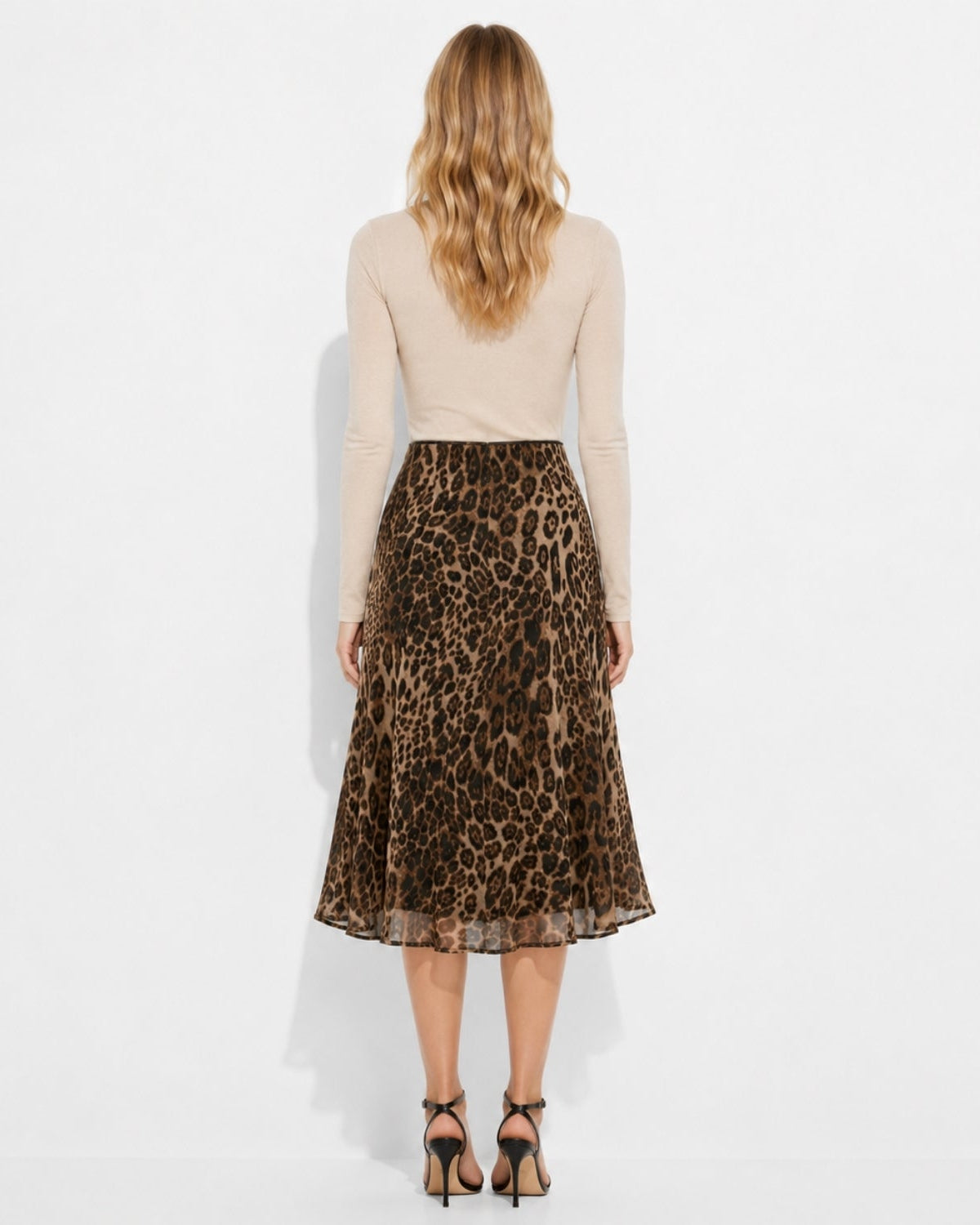 A woman shown from the back wearing a beige long-sleeve top and a brown leopard-print midi skirt, paired with black high-heeled sandals, against a plain white studio background.