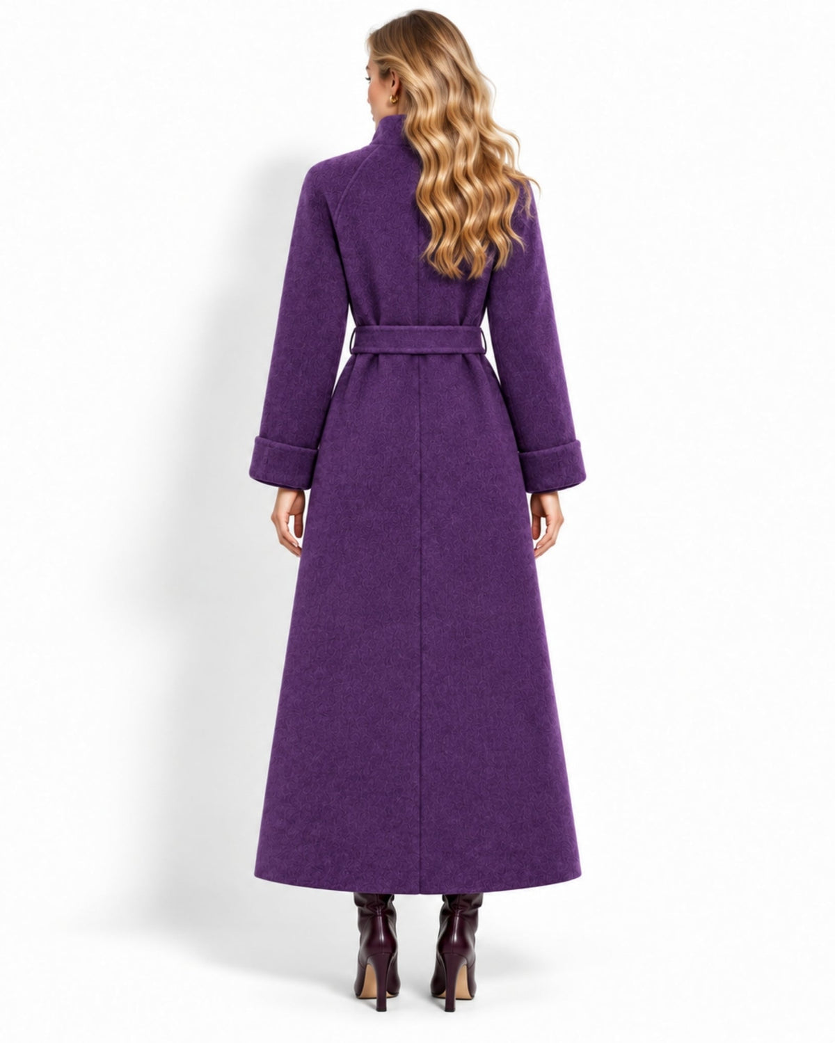 A woman viewed from the back wearing a long purple coat with a matching waist belt, paired with dark pointed-toe heels, against a plain white studio background.
