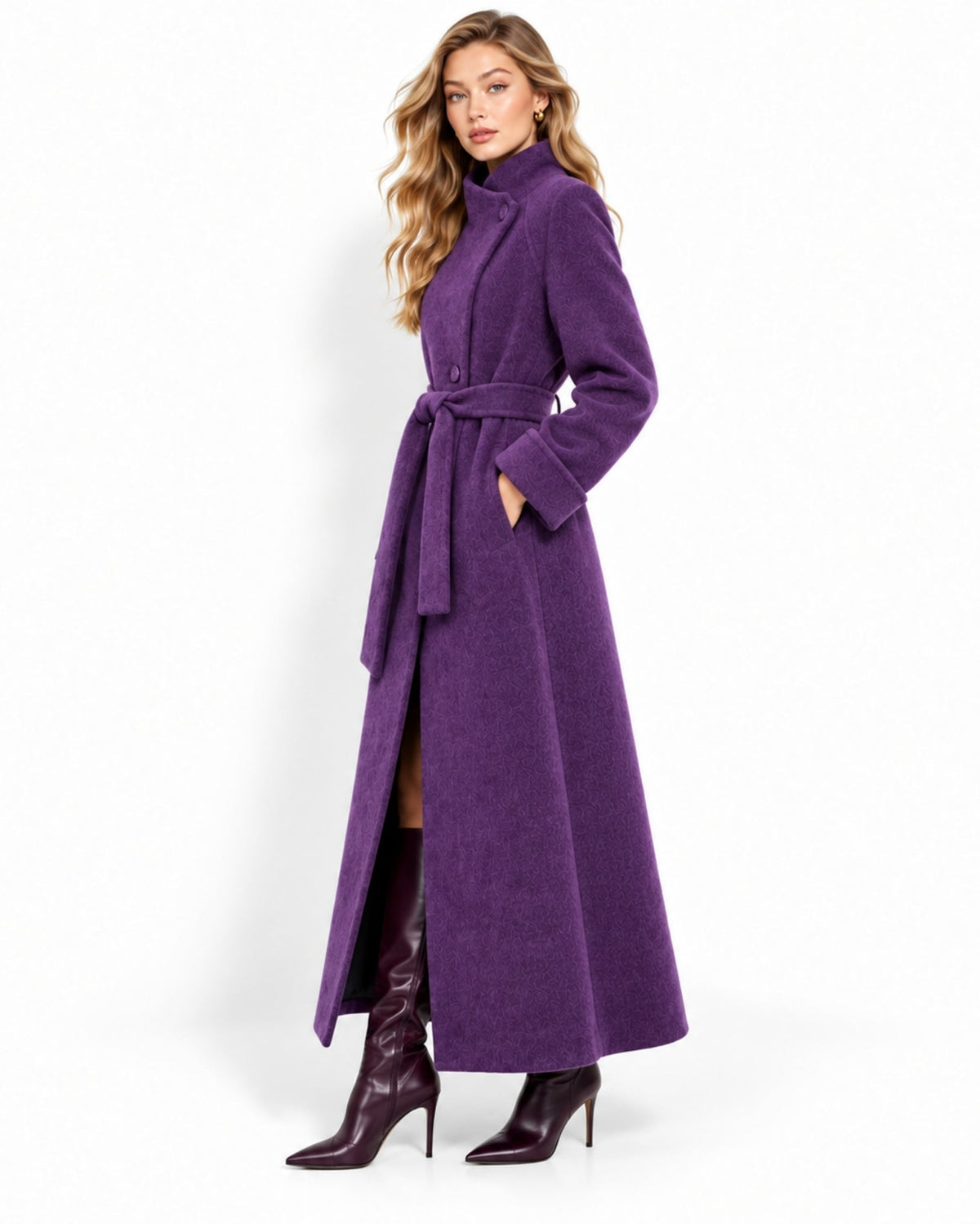 A woman modeling a long purple wrap coat with a high collar, long sleeves, and a matching waist tie, paired with dark brown knee-high boots against a plain white studio background.