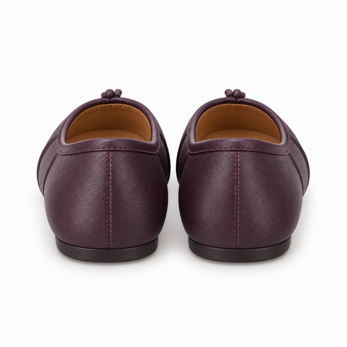 A pair of dark purple leather ballet flats shown from the back, featuring a small fabric tassel detail on the back of the shoe and a tan interior lining, set against a plain white background.