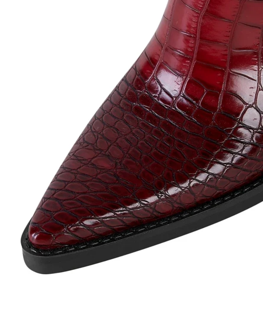 Close-up of a pointed-toe boot in glossy deep red crocodile-embossed leather with a black sole, shown on a plain white background.