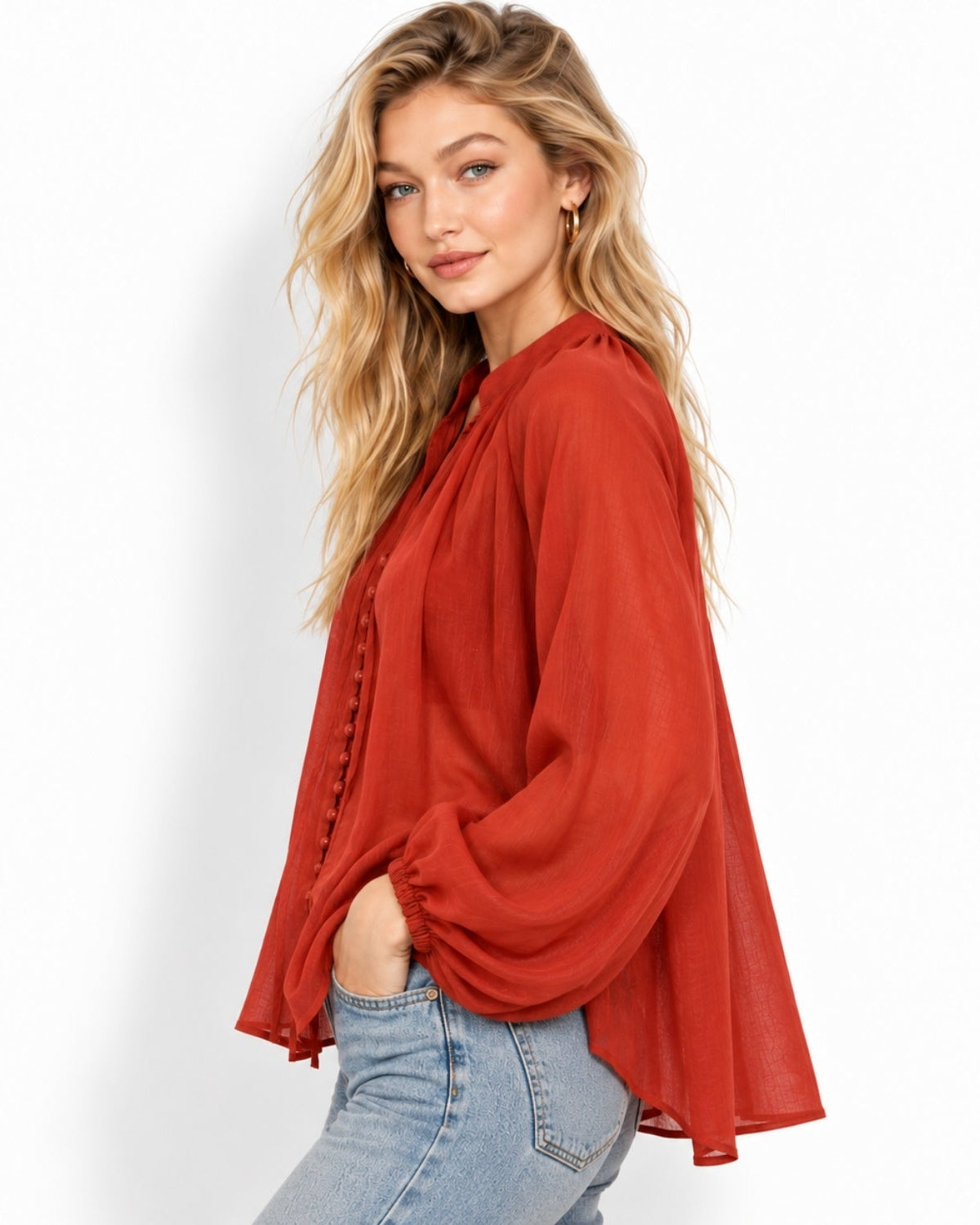A woman modeling a rust-orange long-sleeve blouse with a high-low hem and gathered sleeves, paired with light-wash blue jeans against a plain white background.