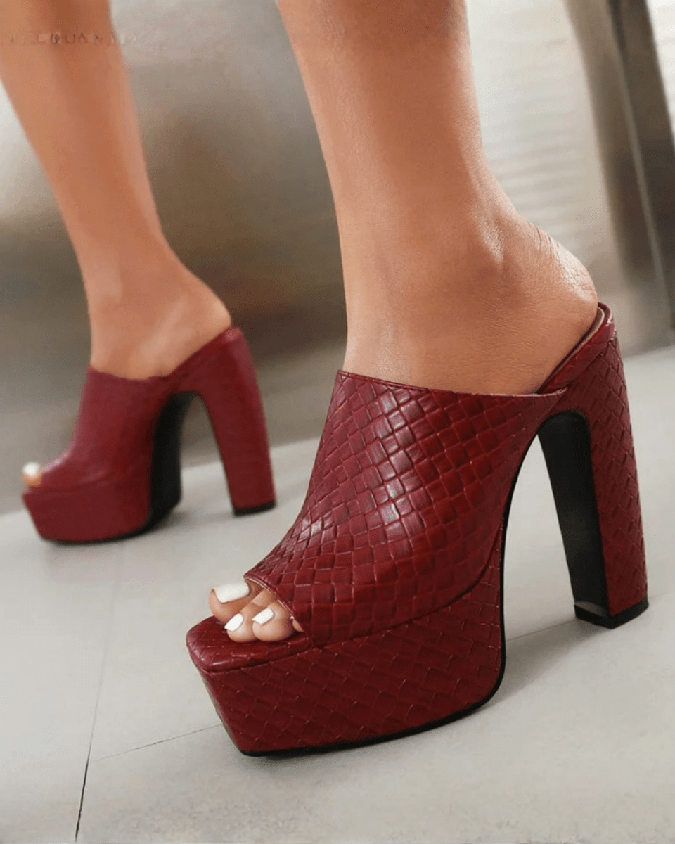A pair of red textured platform mule heels with high block heels, shown on a model's feet against a neutral indoor background.