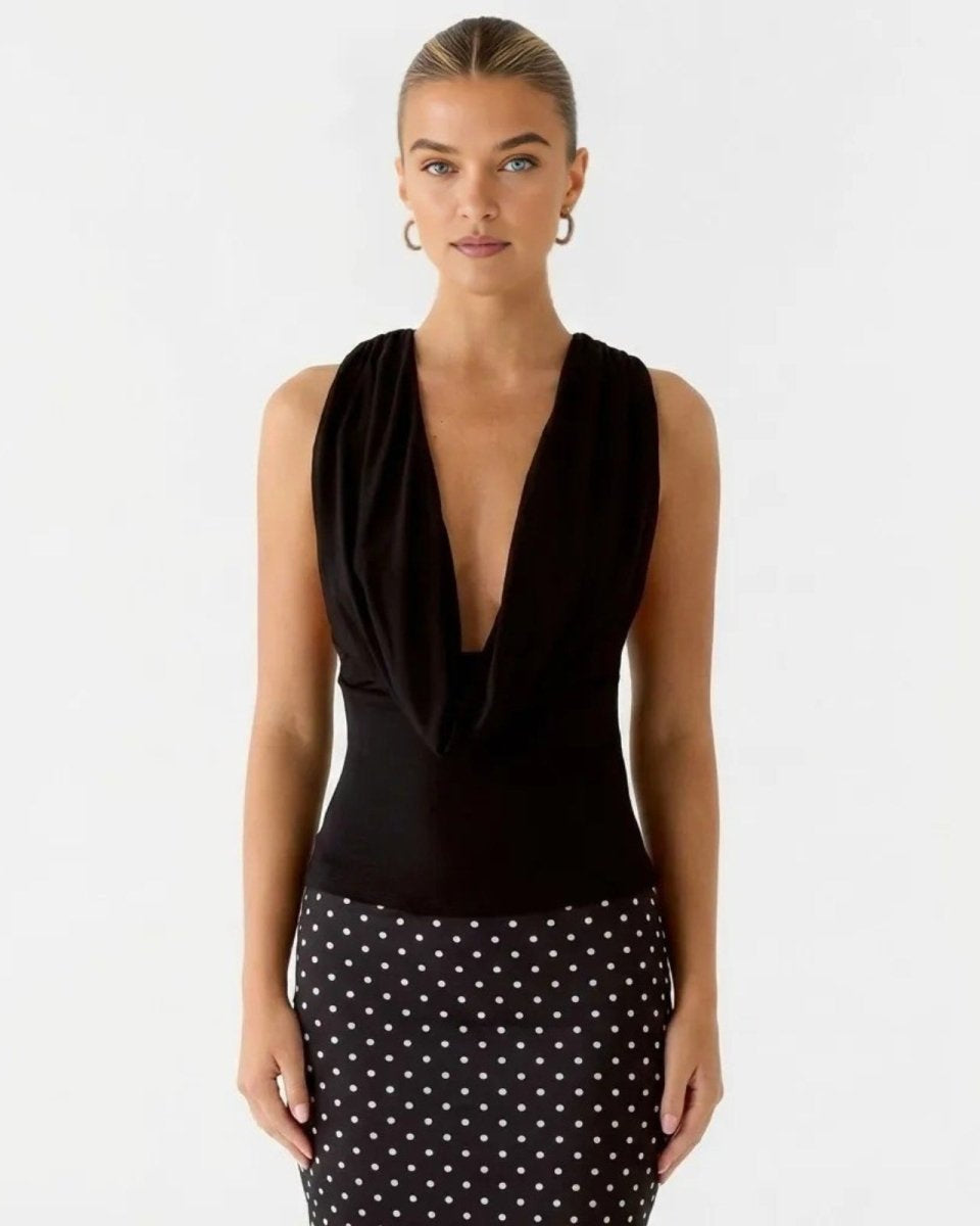 Model wearing the Rhea black sleeveless cowl neck top paired with a black and white polka dot skirt.