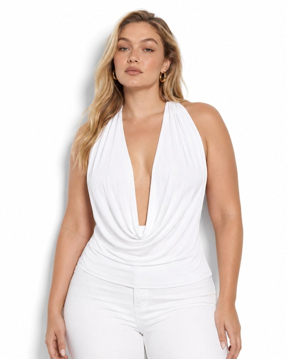 A woman modeling a white halter-neck top with a deep plunging V-neckline and gathered draping details, paired with white pants, against a plain white background.