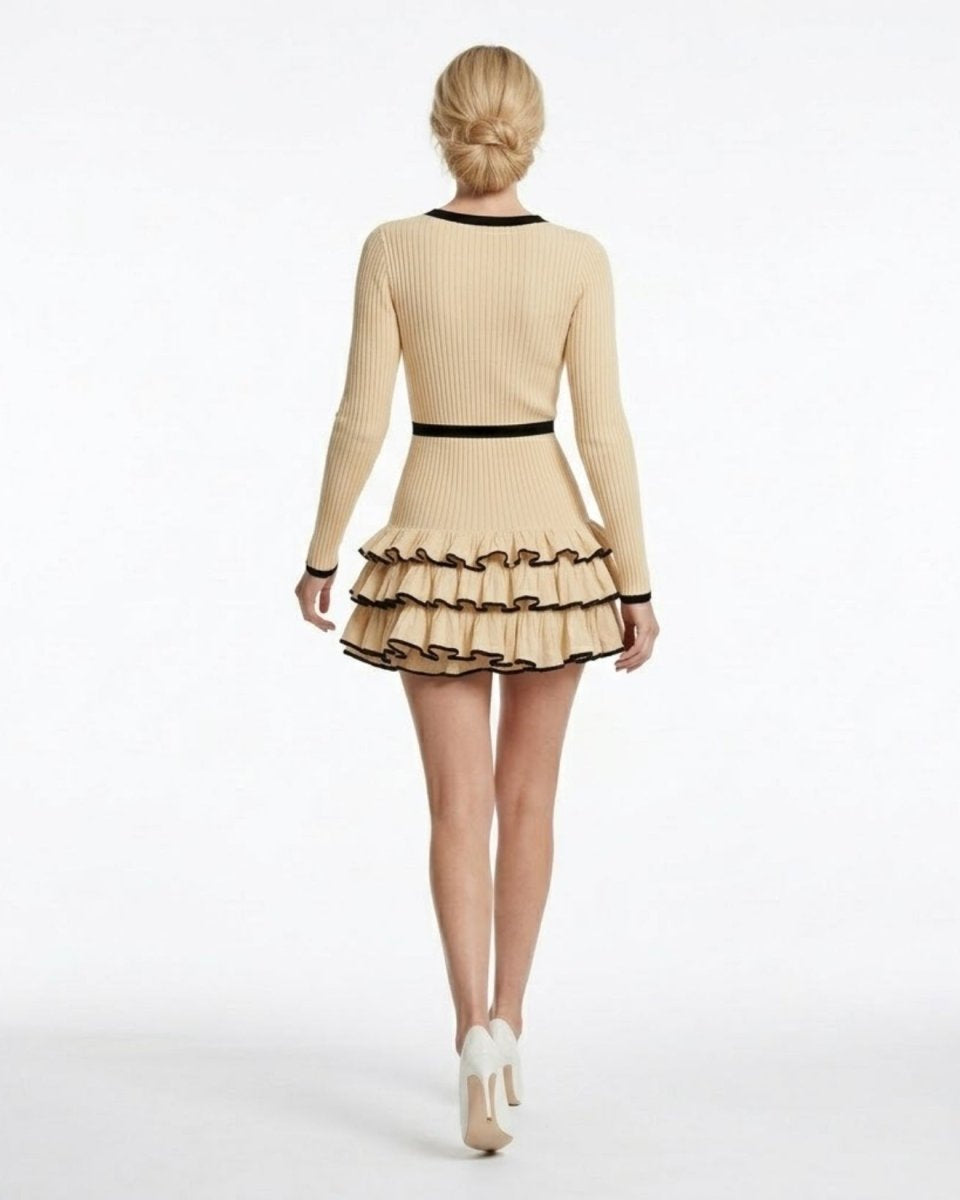 Back view of a beige long sleeve sweater dress featuring a cinched contrasting black waistband and voluminous tiered hem.