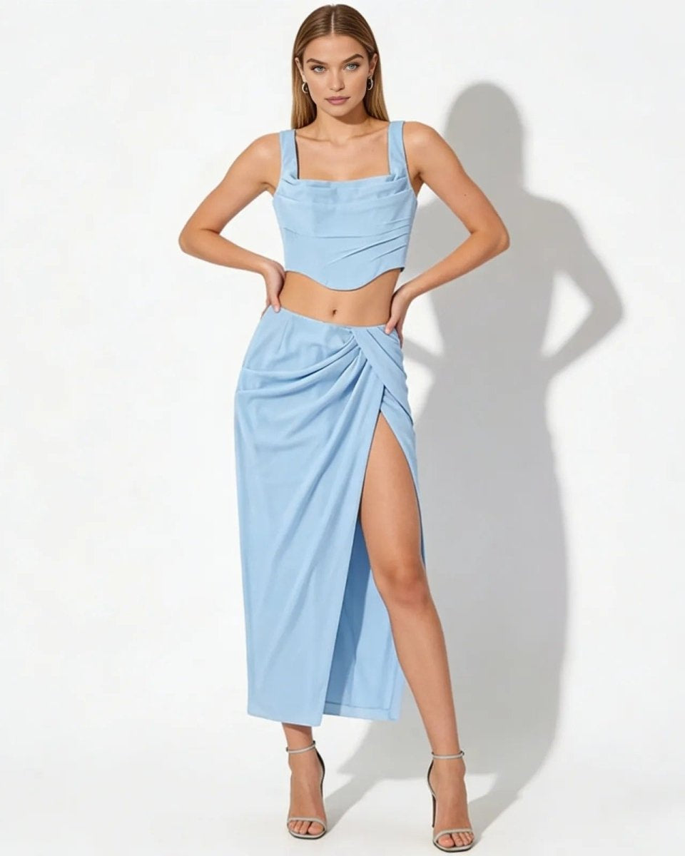 Model wearing the Rona set in light blue, featuring a corset top and a high-slit draped midi skirt, front view.