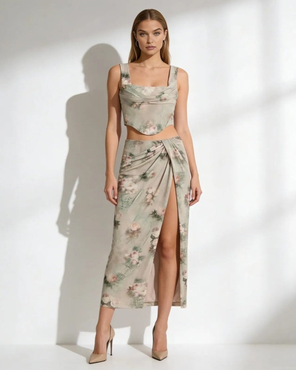Model wearing the Rona set in a sage green floral print, featuring a corset top and a high-slit draped maxi skirt.