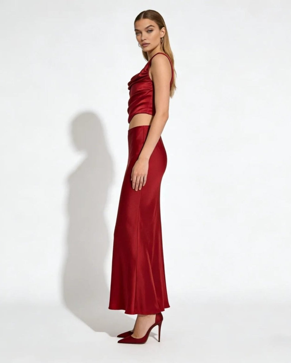 Side view of a model in a red satin cowl neck top and bias cut maxi skirt set, showing the elegant silhouette and drape of the fabric.