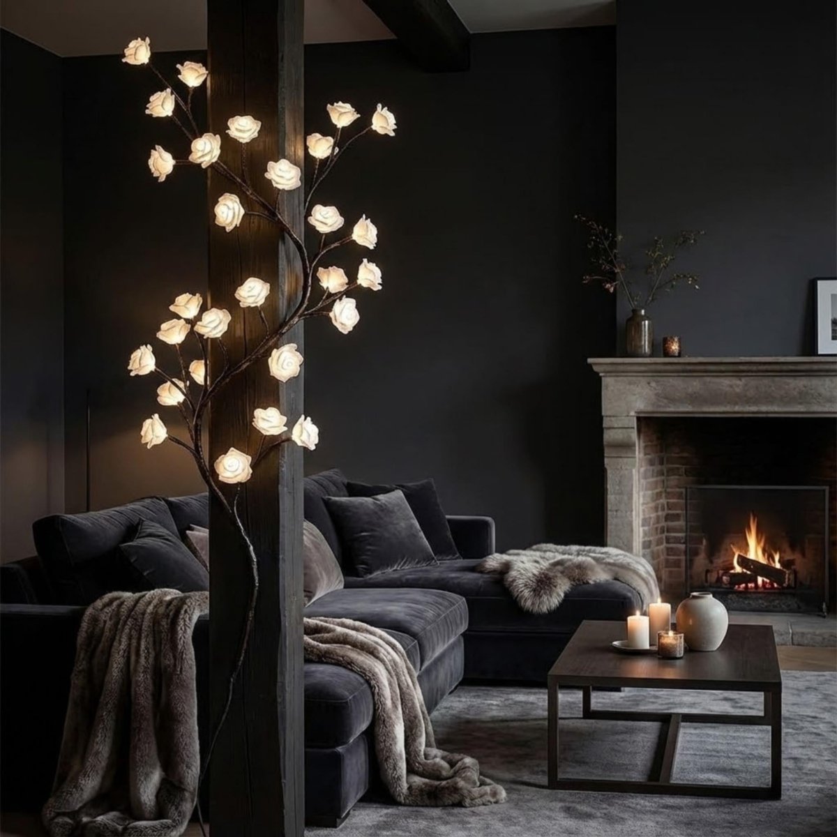 A modern living room with a dark sectional sofa, a glowing decorative tree lamp with paper-like flower branches, a fireplace, and a coffee table with candles.