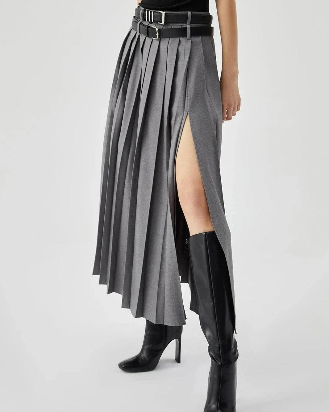 Person wearing a gray pleated skirt with a high slit and black boots on a white background