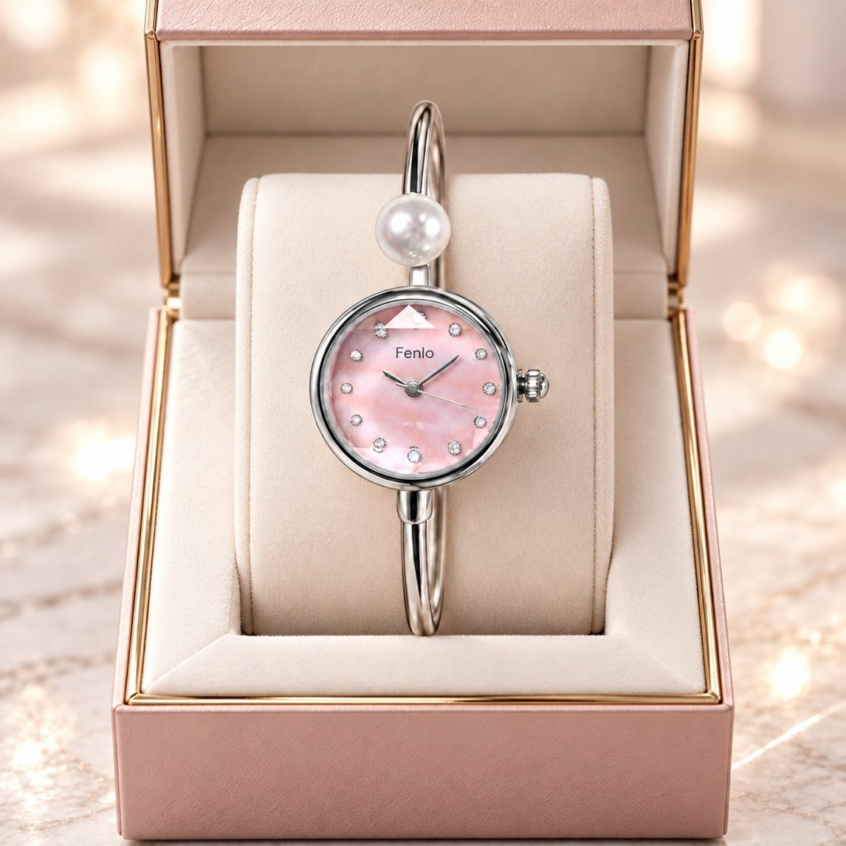 A Feniio women's bangle watch with a pink mother-of-pearl dial and a silver-toned bracelet with a pearl accent, presented inside an open pink jewelry box.