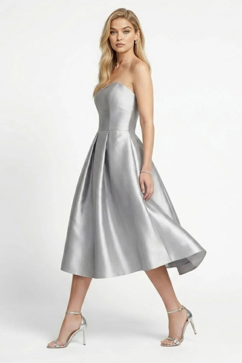 Side angle view of a blonde model walking in a silver A-line structured formal dress with metallic heels.
