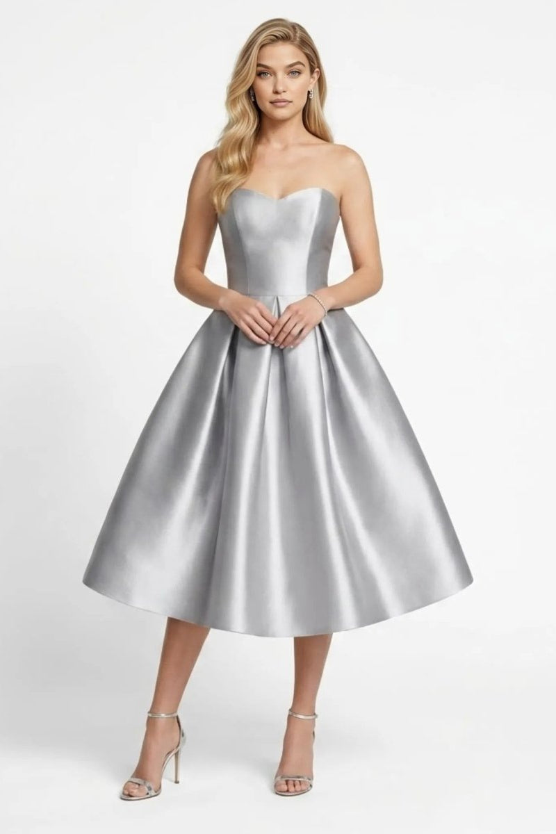 Front view of model wearing a silver strapless satin midi dress with sweetheart neckline and pleated skirt.