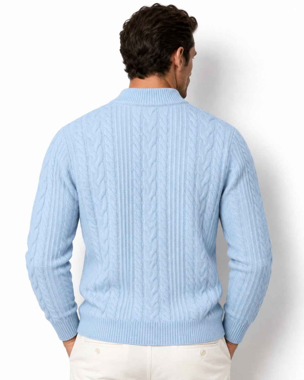 A man viewed from the back wearing a sky blue cable-knit sweater and cream pants against a plain white background.