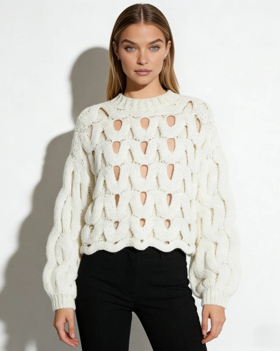 Model facing forward wearing the white cutout chunky knit sweater with black trousers against a white background.